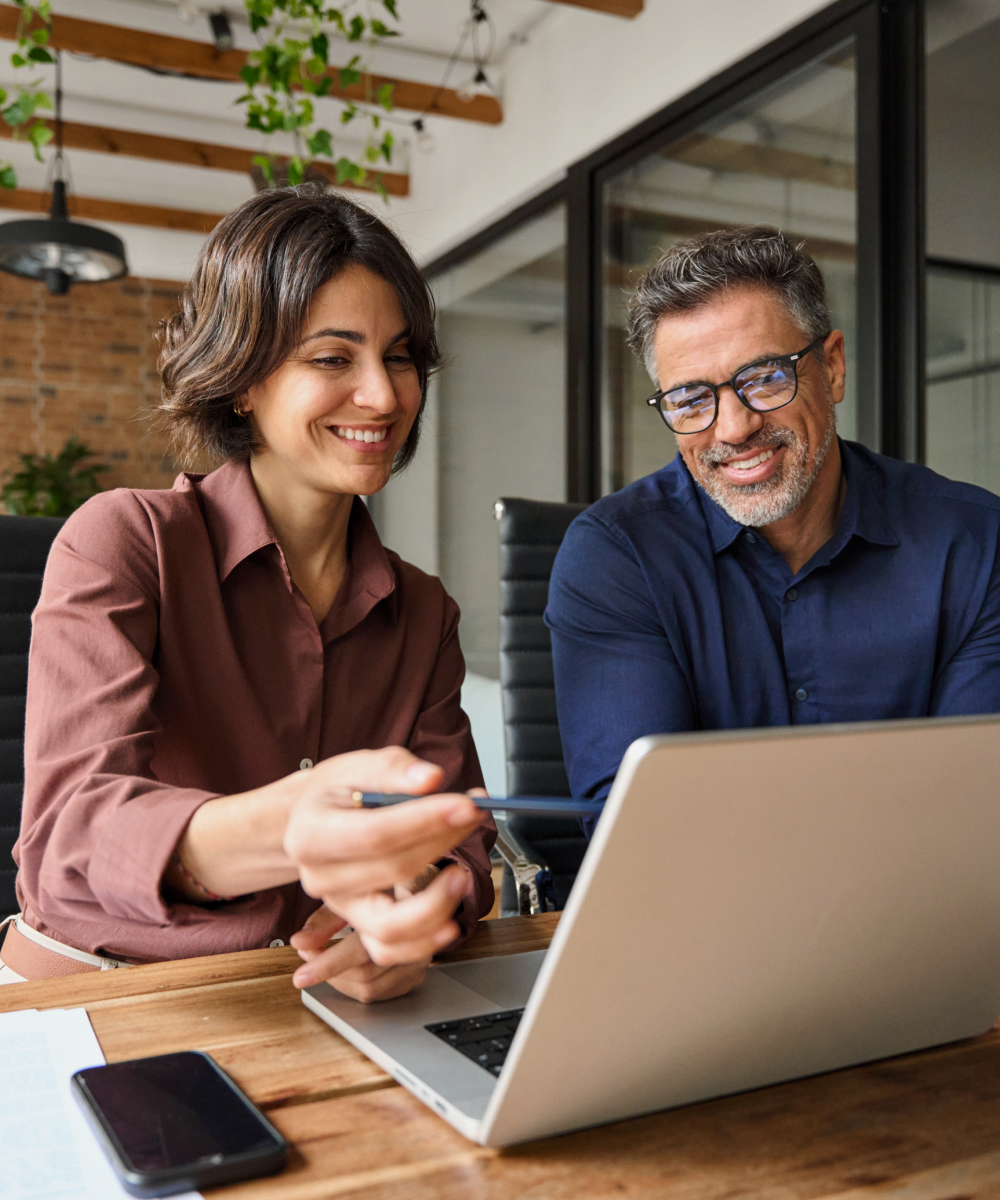 Man and woman smiling while browsing on laptop indoors