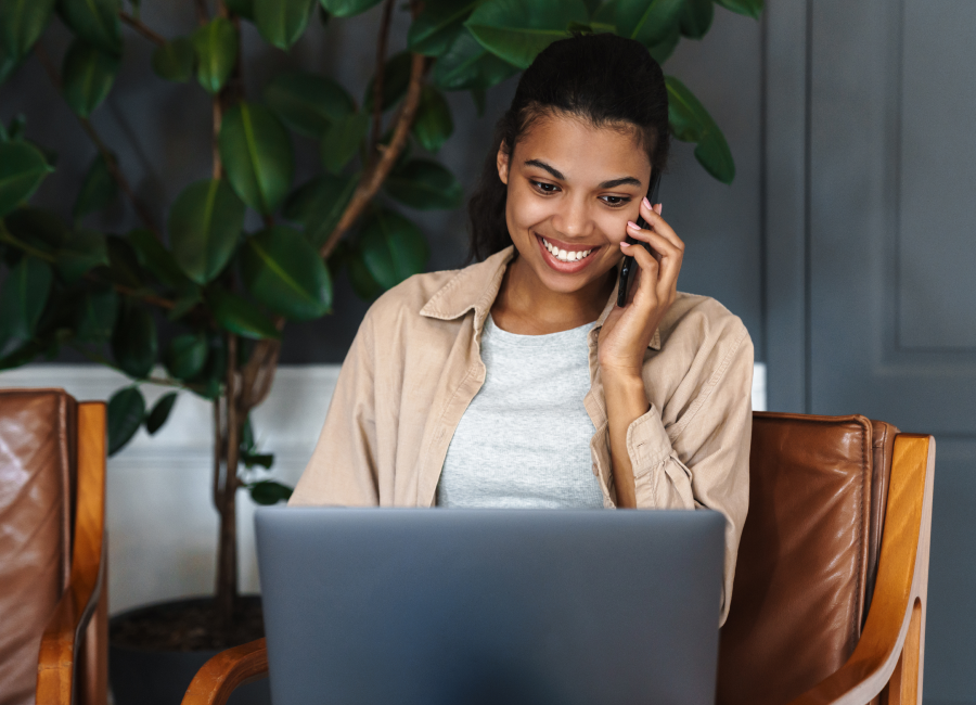 A smiling woman talking on the phone while using her laptop.